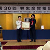 第30回林忠彦賞授賞式。藤井周南市長から初沢さんへ賞状と副賞、ブロンズ像が手渡されました。